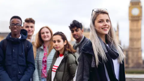 Getty Images A group of teenagers pose for the camera against the backdrop of the Houses of Parliament
