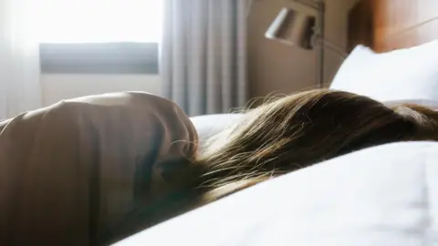 Getty Images The back of a woman's head and shoulder as she lies in a hotel bed.