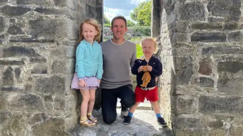 Supplied Mark pictured in the entrance to a grey castle with a young boy and girl who have strawberry blonde hair