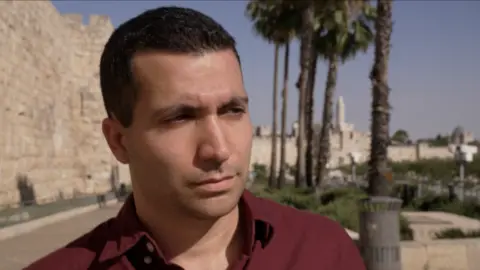 Shai Rosengarten is photographed from the shoulders up. He is clean-shaven and wearing a red shirt while looking off-camera to the left.