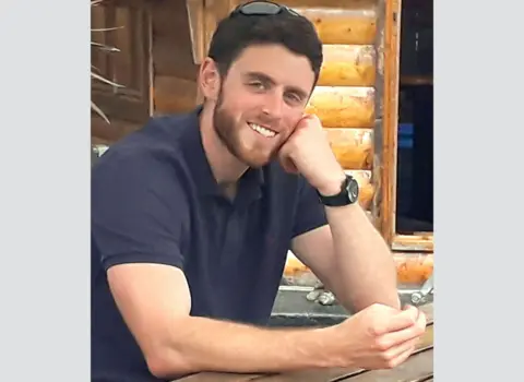 PA Media Police officer Andrew Harper, off duty, with short brown hair and a slight beard wears a navy polo shirt and smiles at the camera.

