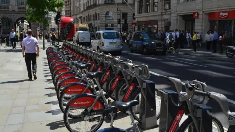 BBC A row of bikes with Santander branding at docking stations in a row on a busy London street. 