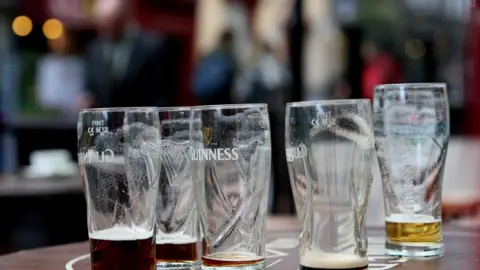 PA Media Five Guiness pint glasses stand on a table, some partially filled with dark liquid. 