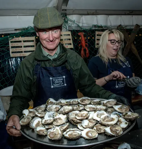 Pete Robinson A man looks smiling at a large tray of oysters