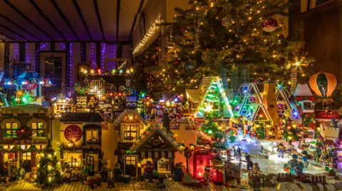 Lots of buildings made from Lego are dotted about. On the right is an ice rink with figures on it, and to the left are houses. 