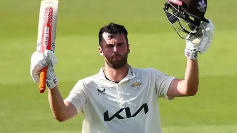 Dom Sibley raises his bat upon reaching a century for Surrey against Durham