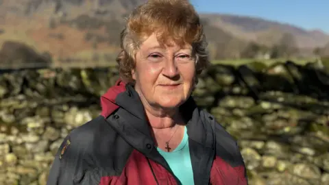 Helen Bell smiling into the camera. She has short, light, curly hair and is wearing a red and black waterproof jacket.