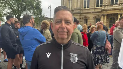 BBC/Crispin Rolfe Man with short hair and black sports top stood in front of a crowd.
