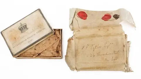 Bearnes Hampton & Littlewood Auctioneers & Valuers A box on the left and the inside of the box on the right. It looks worn and old. The box on the left says "The Queen's Bridal Cake, Buckingham Palace, Feb 10, 1840."