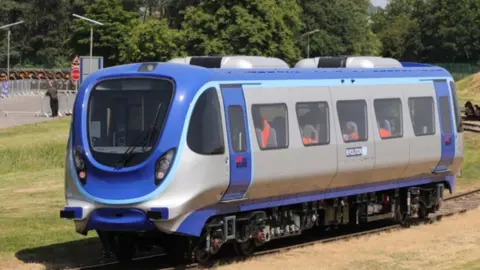 A blue and silver one-carriage train on a track running through a grassy area