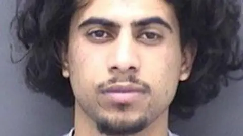 Custody photo of Mohammed Abdullah who has thick black hair and a goatee beard and moustache