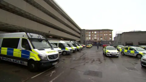 A view of the Charles Cross police station's car park. There are parked police vehicles. To the left is the multi-storey carpark.