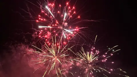 Three red and yellow fireworks exploding in the sky, spraying sparks and smoke outwards.