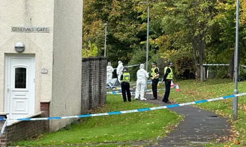 Uniformed police officers and foernsic officers in white overalls standing outside a taped-off house on General's Gate
