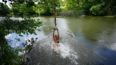 PA Media A woman in the River Avon at Warleigh Weir. She is hanging on to a rope swing. 
