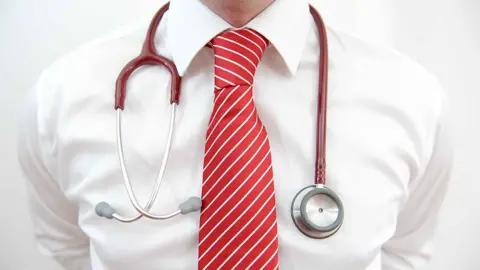 Generic close up of a doctor's chest in a white shirt with a stethoscope around his neck and a red and white striped tie
