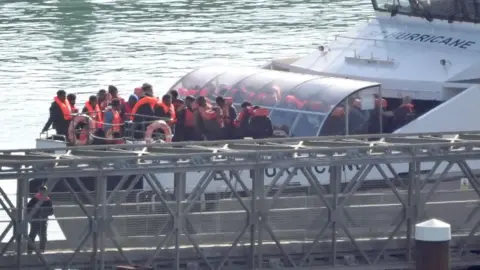 PA Media A group of migrants from small boats wearing life jackets and being brought ashore at Dover on 18 October, on the bow of the Border Force vessel Hurricane.