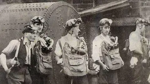An old black and white photograph of men in mining gear.