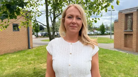 A woman with blonde hair wearing a white top.
