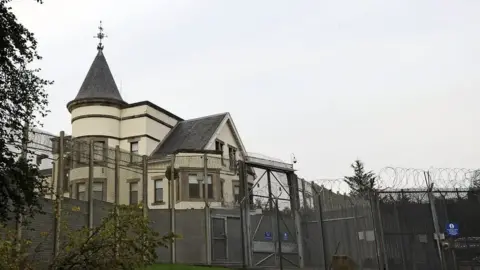 A white building with a turret behind a gated security fence