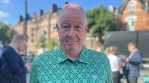 Rab Thomson is a man in his 60s who has grey receding hair and is wearing a green T-shirt