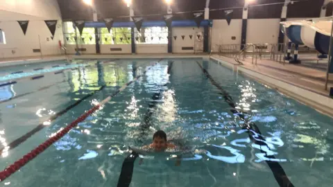 Matthew Grant  A man swimming in Birtley Pool. The pool has several lanes and there are small triangular flags hanging over the pool.