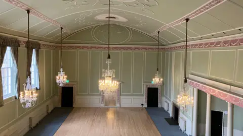 Jon Wright/BBC Inside the Athenaeum's main hall in Bury St Edmunds. It has chandeliers and an ornate high ceiling.