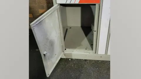 The locker the child climbed into. It is a small grey locker at the bottom of a tower of similar lockers.