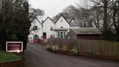 Drive leading up to cars home with purple 'Westacre' sign on grass bank.