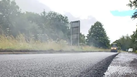 Surrey County Council A steamroller is seen in the background with a layer of tarmac being laid on top of the A24