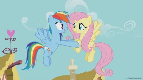My Little Pony cartoon characters Rainbow Dash and Fluttershy hover in midair. Rainbow Dash is re-assuring Fluttershy.