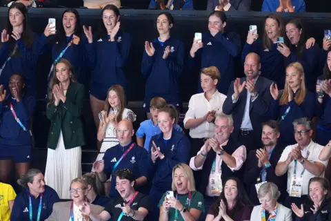 PA Media The royal family stand and applaud along with the rest of a crowd at a netball match