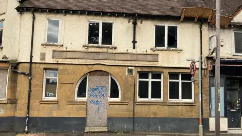 Pete Cooper/BBC One facade of pub showing boarded up door with graffiti