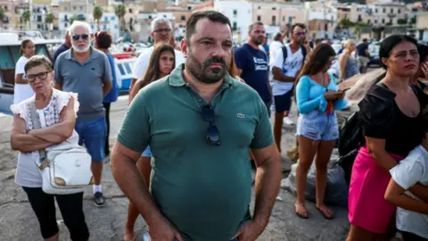 Reuters People gather in the coastal town of Porticello as rescuers move a body bag to the back of a luxury yacht