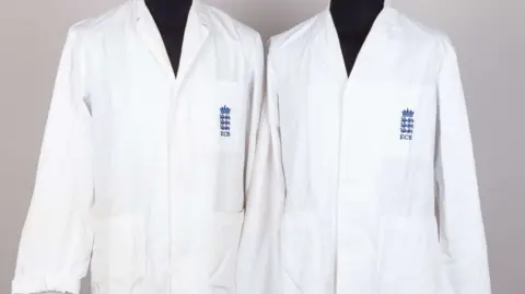 Budds Picture of two umpire jackets, in white. They have the ECB branding stitched to the left hand side on a breast pocket. Two patch pockets are sewn below that.
