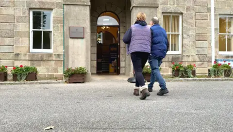 A couple walking in to Alderney’s Island Hall to cast their vote 