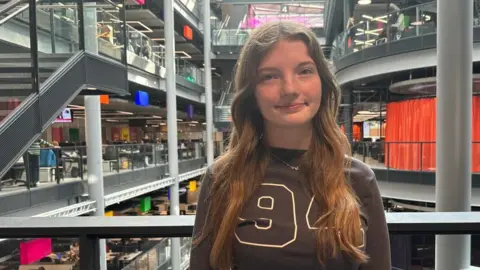 BBC Mia is smiling at the camera. She is stood on the balcony in the BBC Wales building in Cardiff