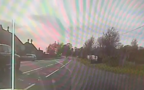A view of a police dashcam with a small motorbike in the distance on a rural road