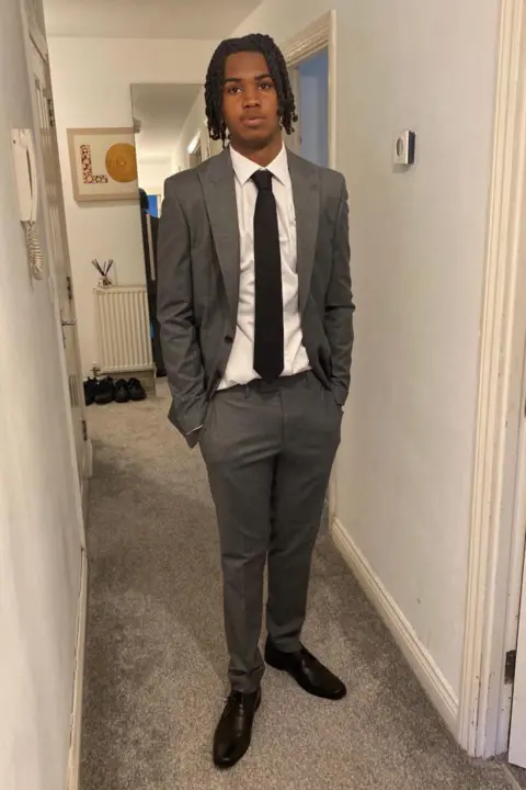 Family handout Kamari Johnson stands in a hallway, dressed smartly in a grey suit, white shirt and black tie