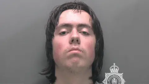 Image released by North Wales Police of 18-year-old Tristan Roberts. He has shoulder length black hair, is expressionless and looks straight at the camera.