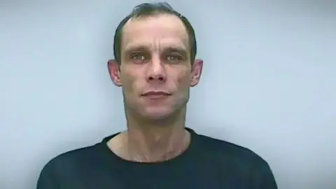 Wiltshire Police Mugshot of Christopher Halliwell. He has short dark hair and is wearing a dark shirt.