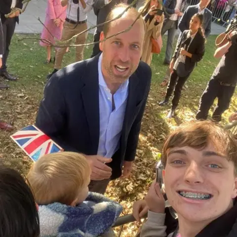 Thomas Croft  Thomas Croft, who has light brown hair and is smiling, takes a selfie with Prince William outside Birtley Community Pool.