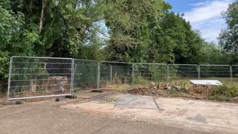 A concrete space with temporary metal wire fencing round the edge.