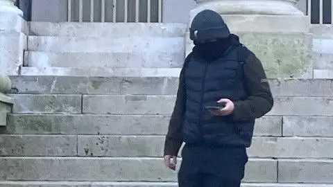 Luke Silver wearing a black hat and a black Gillet. His face is covered.