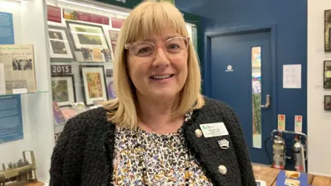 Kate Bradbrook/BBC Helen Howell with long blond hair wearing a dark-coloured cardigan with a name label