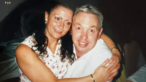 Joy Walters Joy, who has long curly hair and wears a sleeveless floral dress, in the arms of a man wearing a white shirt