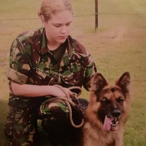 Mandy Small RAF veteran Mandy Small is wearing military fatigues and holding the leash of an Alsatian dog. 