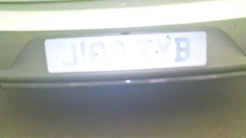 Wolverhampton Council A blurry number plate on a car. The middle portion of the plate cannot be read because light is reflecting from it.