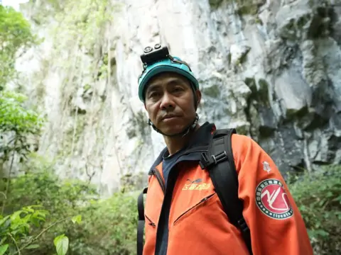 Xiqing Wang/ BBC Brother Fei dengan jaket oranye dan helm biru 