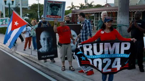 Getty Images People hold photographs of political prisoners being held in Cuban jails during a demonstration in support of the protesters in Cuba on March 18, 2024, in Miami, Florida. They also hold up signs saying "Trump 2024"
